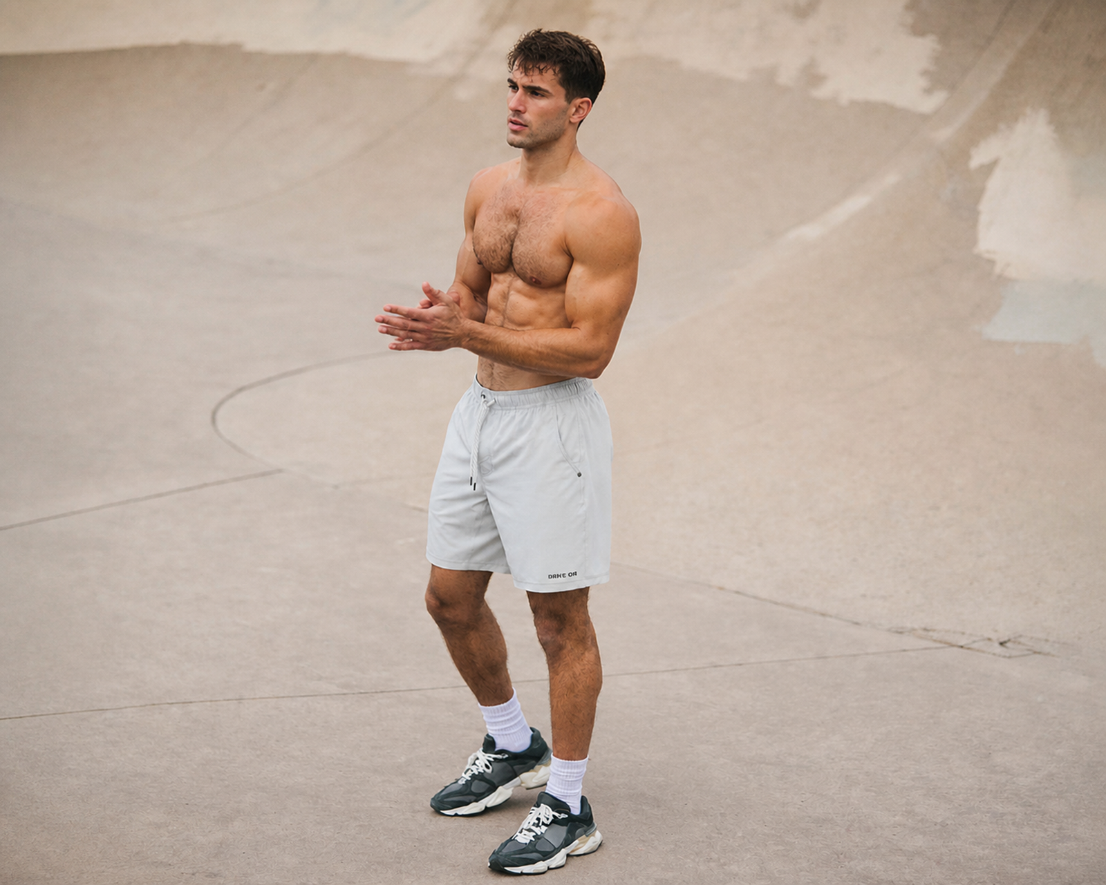 Shirtless man in white athletic shorts clapping his hands in a concrete skate bowl