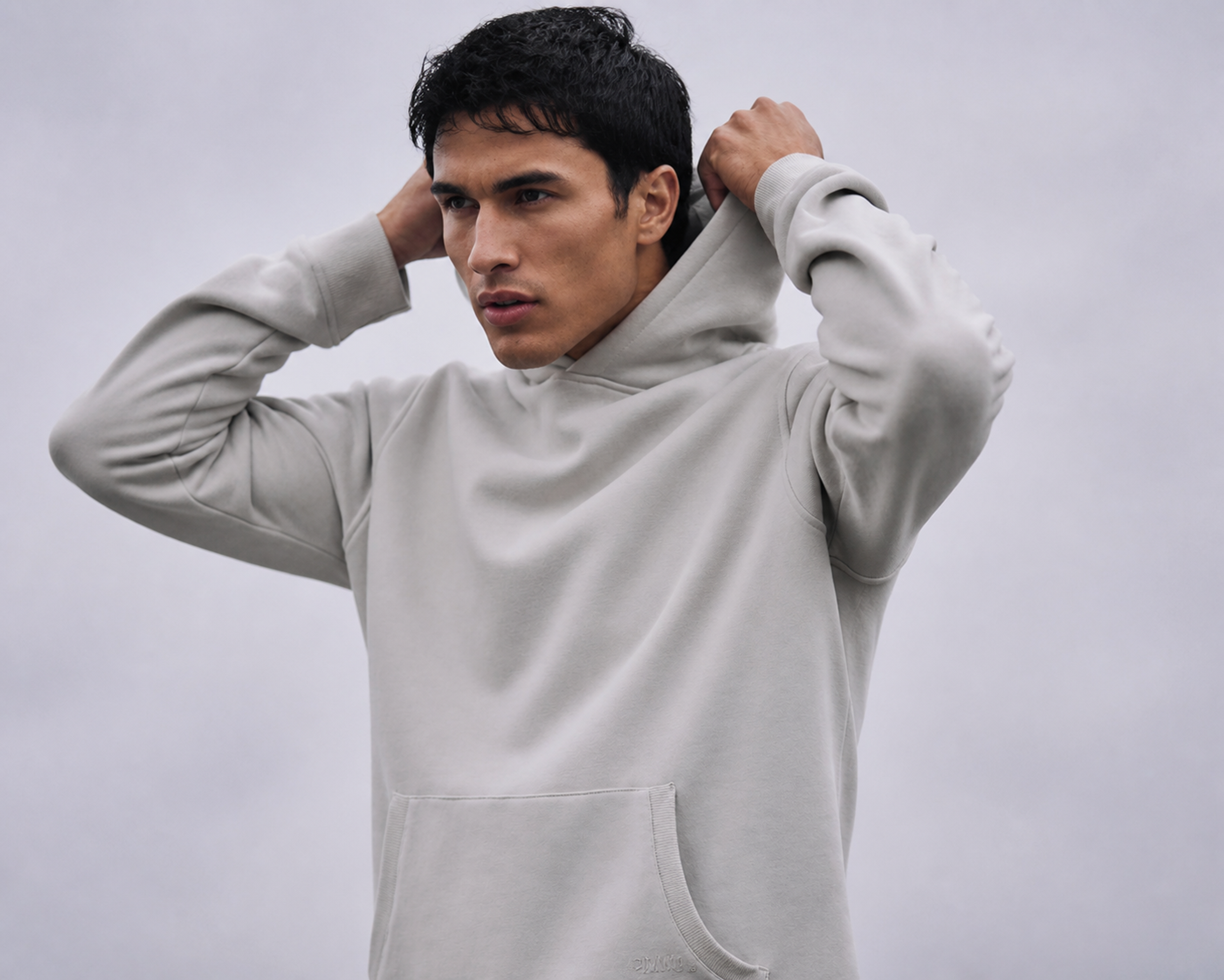 Man in a light grey pullover hoodie, hands adjusting the hood
