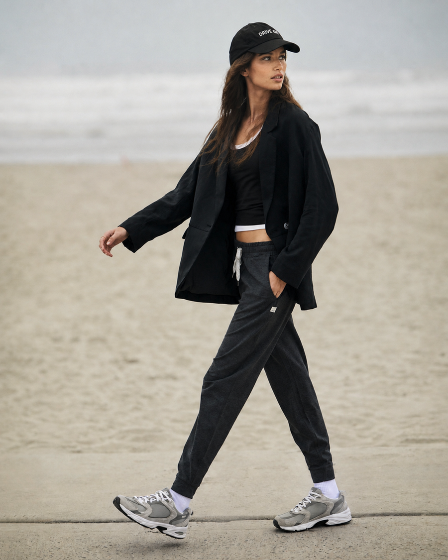 Woman in a black coat and joggers walking along a beach boardwalk