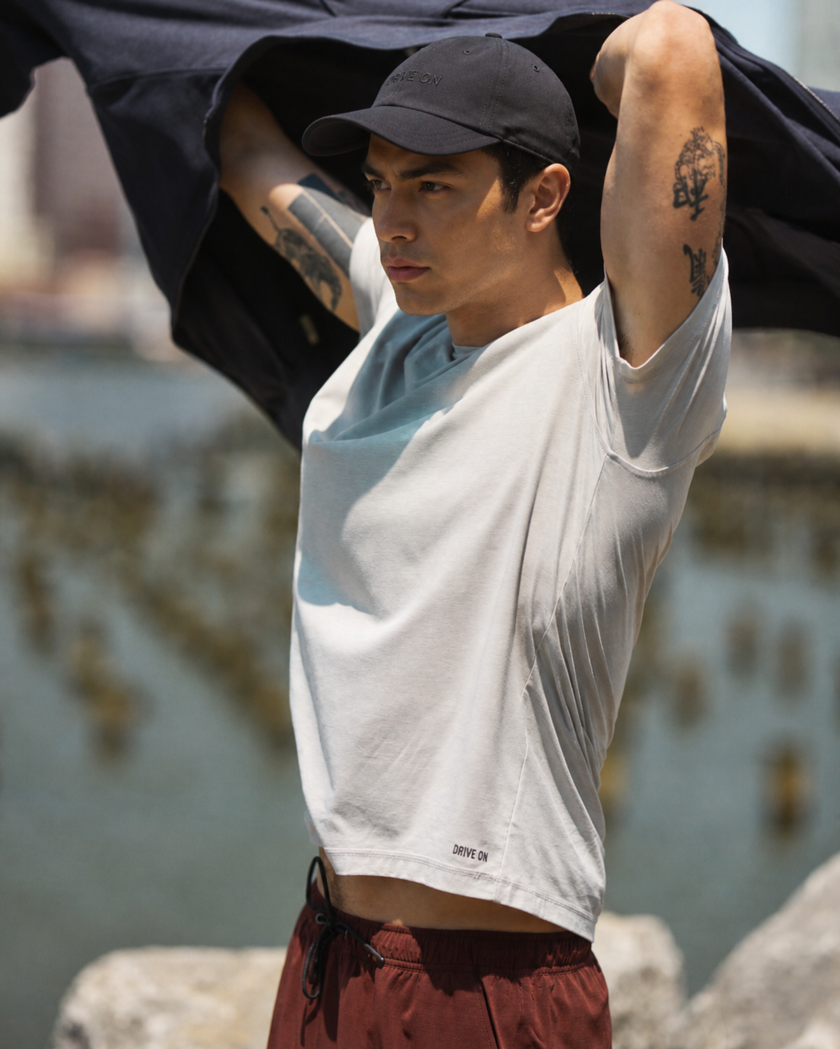 Man in a white tee and maroon shorts caught in motion by the water, wind pulling a dark jacket overhead