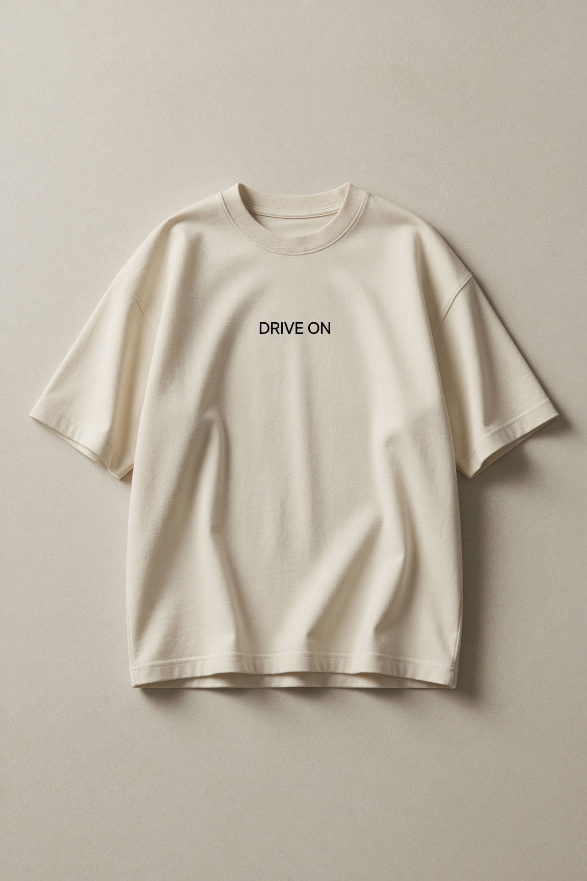 The cream tee laid flat on a warm grey ground, DRIVE ON printed small at the chest
