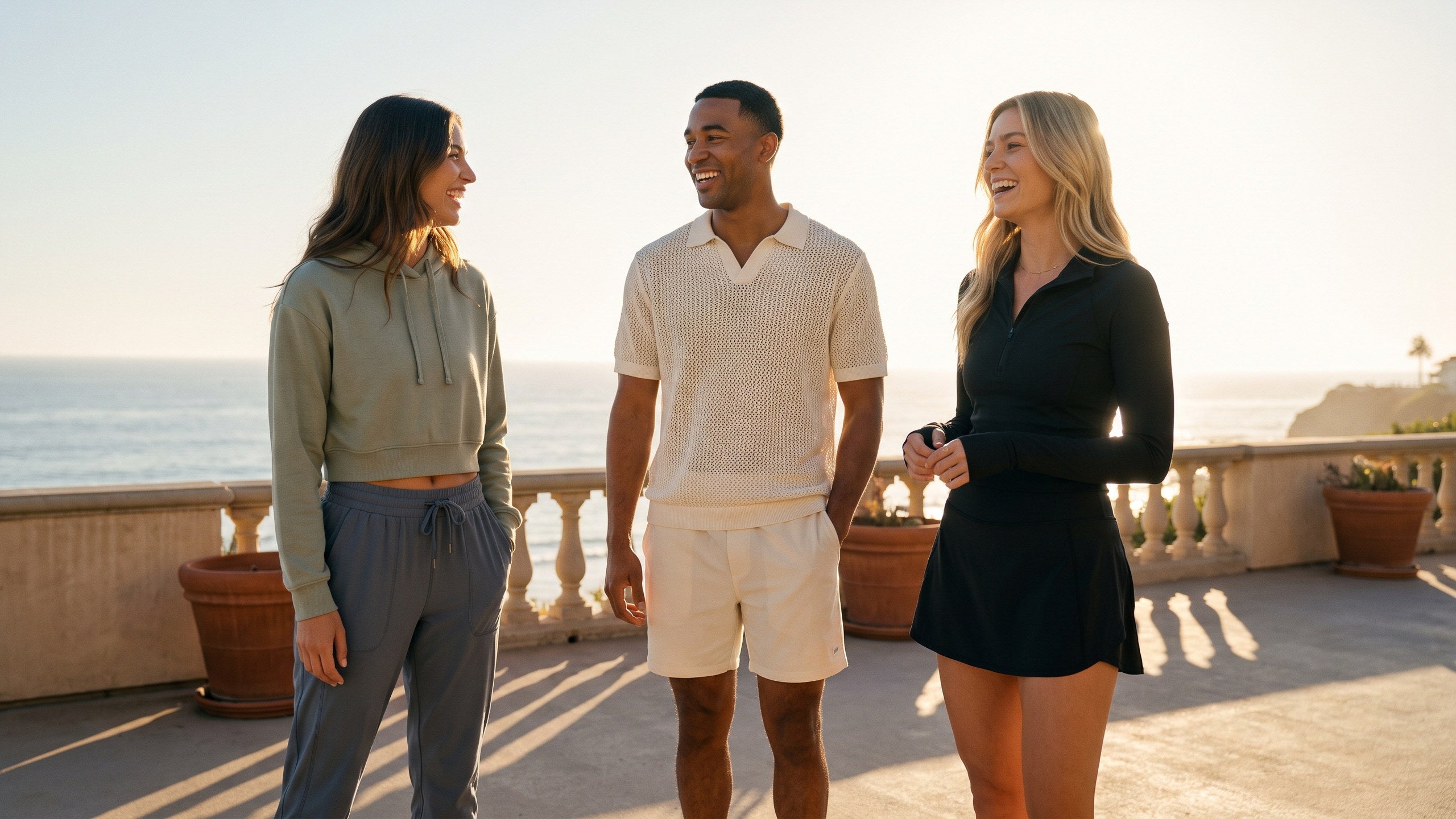 Three people talking on a coastal terrace at sunset, their outfits in the same colors