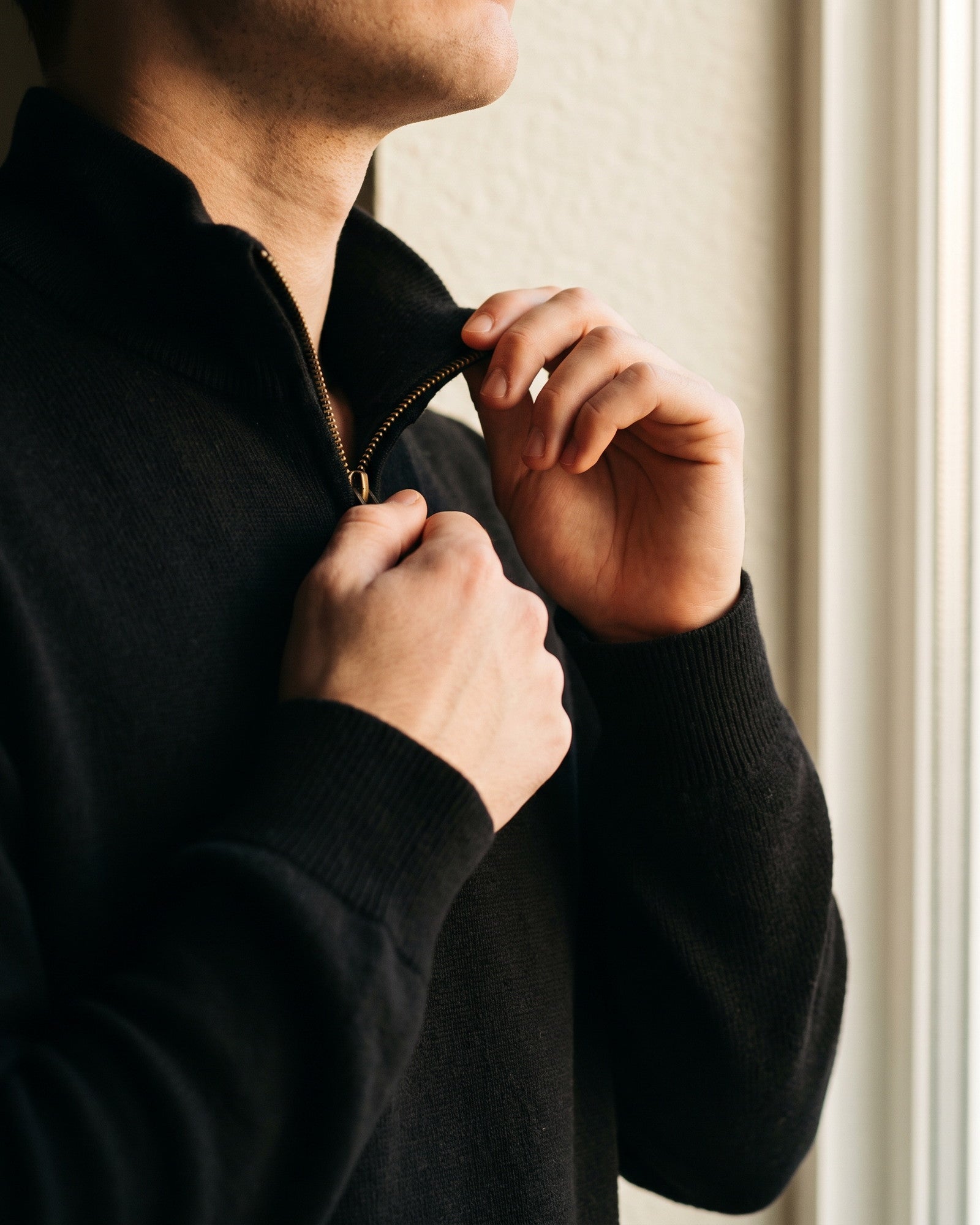 Close crop of hands drawing the zip of a black quarter-zip halfway up