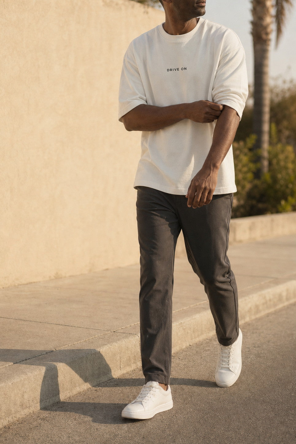 The Cream Graphic Tee worn open-hemmed on a sunlit pavement, DRIVE ON printed small at the chest