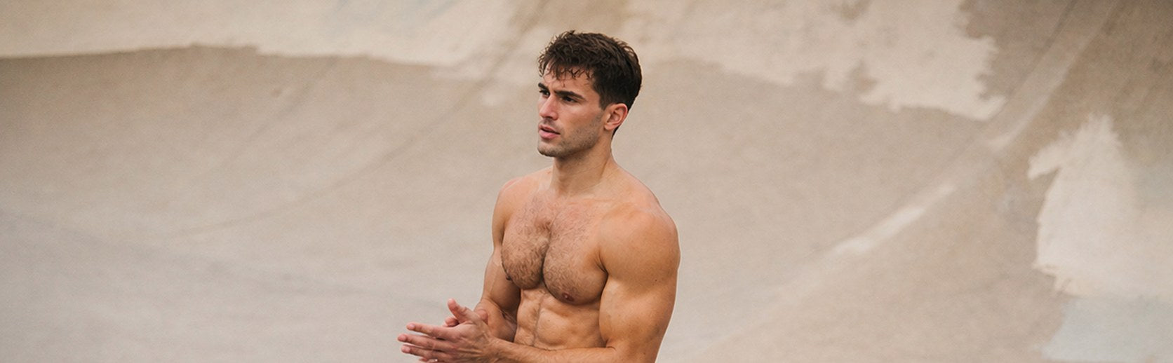 Shirtless man in white athletic shorts clapping his hands in a concrete skate bowl